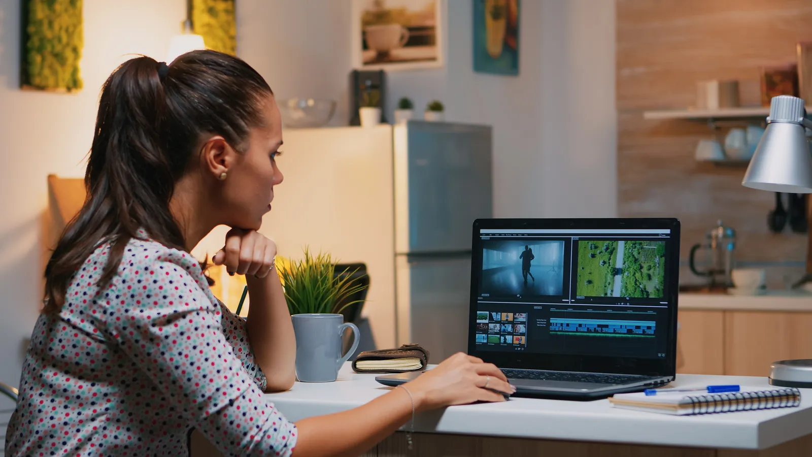 An editor working late at a laptop on a kitchen table, a video timeline on screen