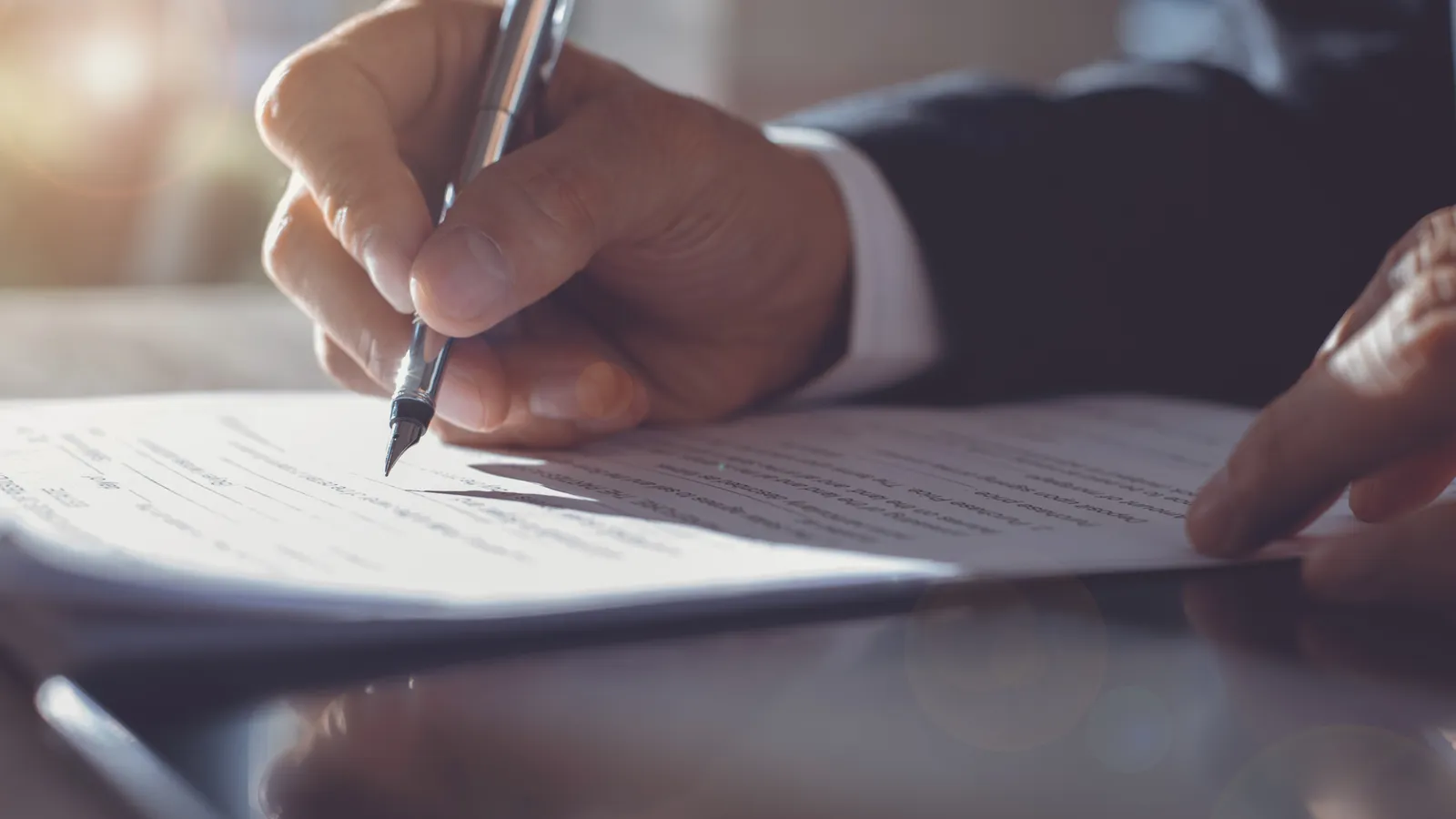 A hand signing a printed contract with a pen