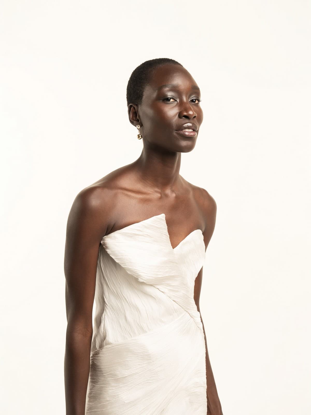 A model in a sculptural ivory gown against a warm white studio backdrop